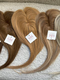 Three hair Toppers with tags on a textured surface